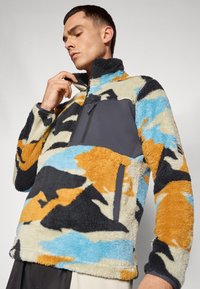 Pullover in pile con colletto alto, caratterizzato da un motivo mimetico multicolore texturizzato in beige, blu, nero e arancione; include una tasca sul petto con zip.