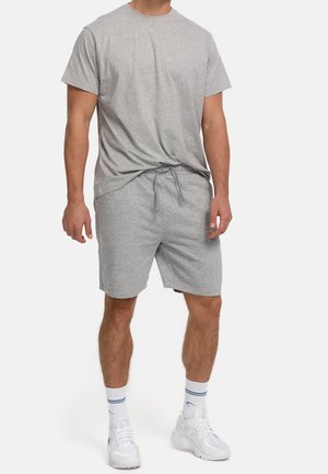 Homme portant un t-shirt à manches courtes gris clair et un short à cordon assorti, avec des baskets blanches et des chaussettes de sport blanches.