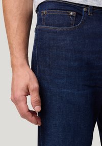 Donkerblauwe denim jeans met een vijf-pocket ontwerp, voorzien van bronzen klinknagels en contrasterende stiksels op de naden, met een soepele textuur.