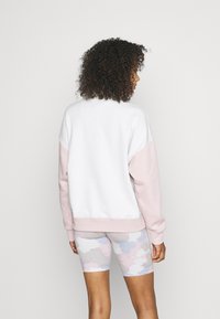 Sweatshirt en mélange de coton avec un corps blanc et des manches rose pâle, présentant un ourlet et des poignets côtelés. Assorti à des shorts de vélo pastel à motifs.