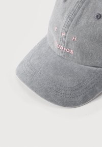 Γκρι καπέλο μπέιζμπολ με ροζ κεντημένα γράμματα "CPH STUDIOS" στο μπροστινό μέρος, εμφανιζόμενο σε λευκό φόντο.