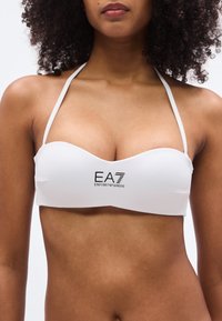 Λευκό μπαντέο μπικίνι τοπ με ομαλή υφή, με το λογότυπο EA7 Emporio Armani σε μαύρο, ρυθμιζόμενους ιμάντες και καμπύλο σχέδιο.