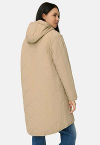 Beige quiltet jakke med hætte, med et diamantmønster, lange ærmer og en afslappet pasform, der er lidt længere bagpå.