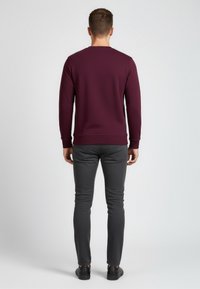 Bordeauxfarbener Sweatshirt, Rundhalsausschnitt, gerippte Bündchen und Saum. Kombiniert mit grauen, schmal geschnittenen Hosen und schwarzen Schuhen. Schlichte Textur ohne Muster.