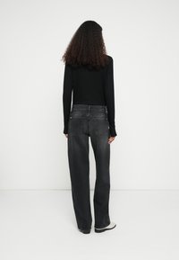 Blugi negri cu talie înaltă și croială largă pe picior, cu buzunare în spate și estompare subtilă, asortați cu un top negru cu mâneci lungi și încălțăminte de culoare deschisă.