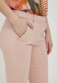 Ljust rosa skräddarsydda byxor med en mjuk textur, som har framfickor och en ren design på midjebandet. Matchas med en mönstrad topp.