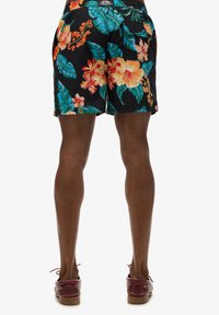 Bañadores negros con estampado floral que presentan vibrantes patrones tropicales con grandes flores y hojas. Cintura elástica, bolsillos laterales y longitud por encima de la rodilla.