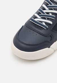 Sneaker in pelle blu navy con lacci bianchi, texture liscia e dettagli perforati sulla punta, dotato di suola in gomma bianca a contrasto.