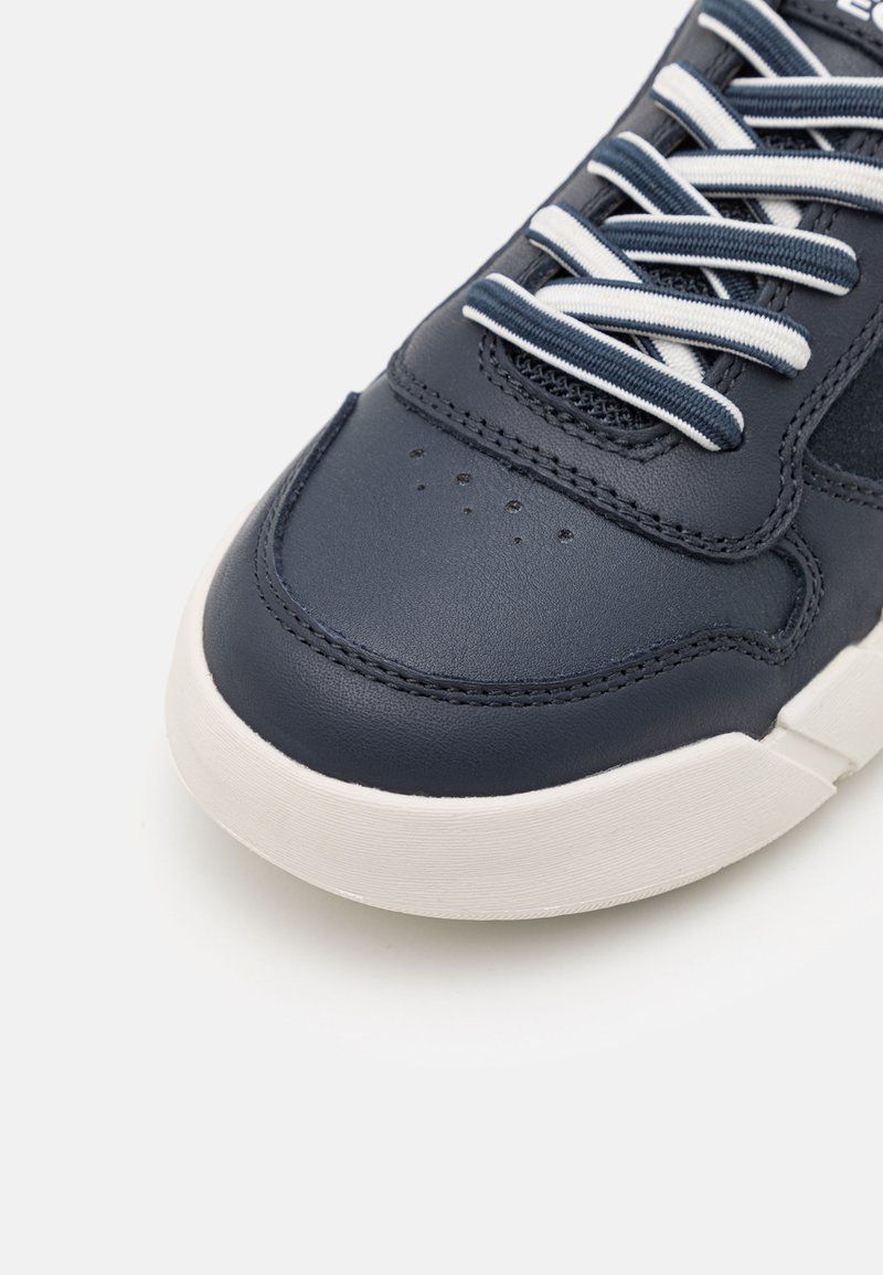 Zapatillas de cuero azul marino con cordones blancos, textura suave y detalles perforados en la puntera, con una suela de goma blanca en contraste.