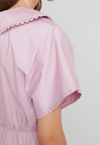 Vestito di cotone rosa con colletto rotondo e bordi scallop, maniche corte a puff e vita elasticizzata. Texture liscia e leggera.