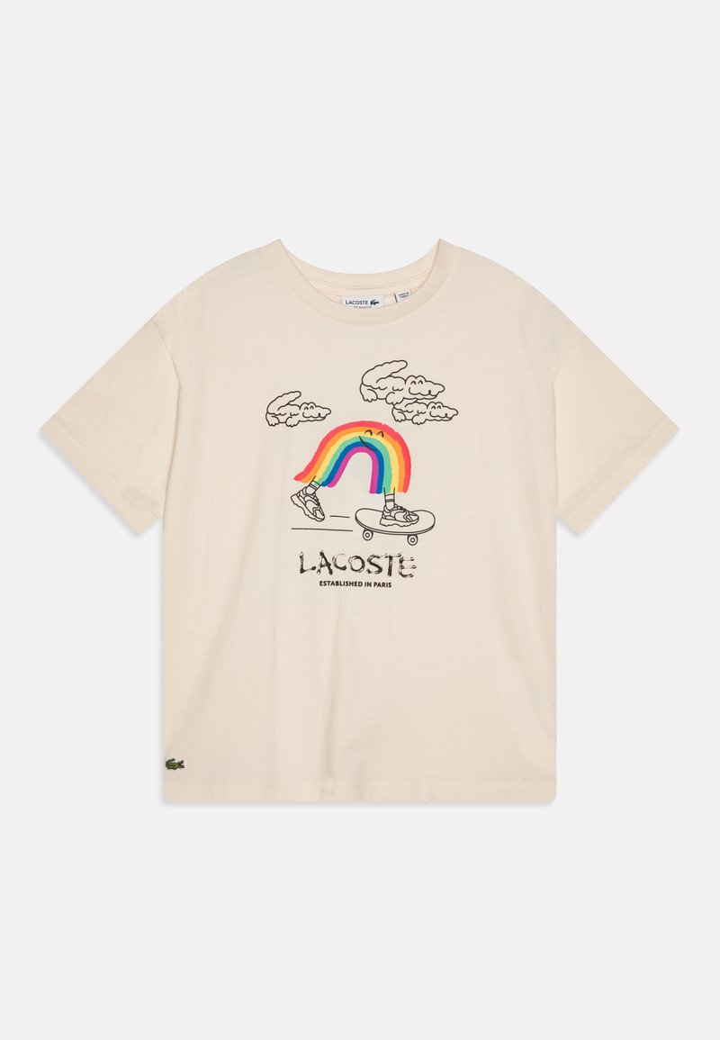 Krémové bavlněné tričko s hravým grafickým designem, který zobrazuje duha, mraky a tenisky. Obsahuje text a logo "Lacoste".