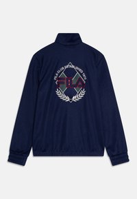 Giacca blu navy con colletto alto, caratterizzata da un logo FILA ricamato, una corona dorata e il testo "FILA CLUB FONDATO NEL 1973." Polsini elasticizzati.