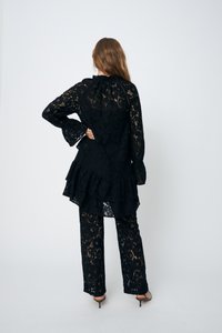 Completo in pizzo nero composto da una lunga maglia sbuffata e pantaloni abbinati, che presenta elaborati motivi floreali e maniche a campana.