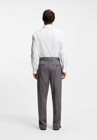 Grijs geruite broek met een getailleerde pasvorm, voorzien van twee achterzakken en riemlussen, gecombineerd met een wit overhemd met lange mouwen.