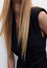 Černé bezramínkové šaty s překládaným designem a uvázaným pasem, vyrobené z hladkého materiálu. Dlouhé rovné vlasy částečně viditelné.