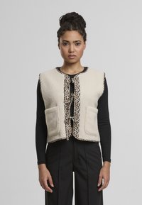 Krémová fleecová vesta s leopardím potiskem, která má dvě přední kapsy a zavazování. Bez rukávů, s kulatým výstřihem.