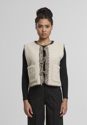 Gilet in pile di colore crema con rifiniture a stampa leopardata, dotato di due tasche frontali e chiusura con laccio. Design senza maniche con collo rotondo.