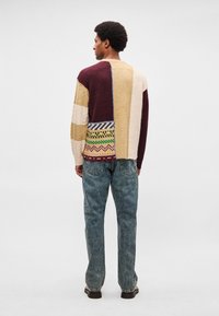 Mitmevärviline kootud kardigan, millel on burgundi, beeži ja kreemika tooniga erinevad mustrid. Omaduseks lõdva istuvuse ja soonikuline tekstuur, kombineeritud siniste teksapükstega.