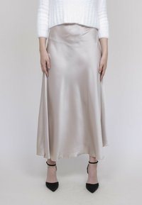 Jupe midi en satin de couleur beige doux, présentant une silhouette fluide avec une texture lisse. Talons noirs à bouts pointus avec des brides de cheville.