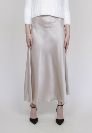 Jupe midi en satin de couleur beige doux, présentant une silhouette fluide avec une texture lisse. Talons noirs à bouts pointus avec des brides de cheville.