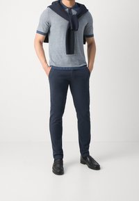 Polo a maniche corte a righe in azzurro chiaro, con accenti blu navy, abbinato a pantaloni tailored blu navy e scarpe eleganti nere. Maglione appoggiato sulle spalle.