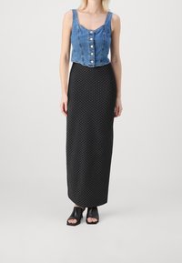 Top de denim recortado con botones; falda larga negra con lunares; combinado con zapatos negros de punta abierta. Texturas de tela suaves, diseño ajustado.