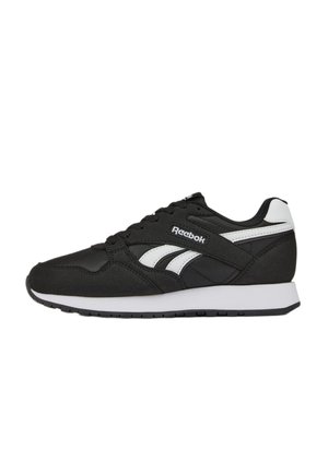 Zapatilla Reebok en blanco y negro con franjas laterales blancas, cordones negros y suela blanca, vista desde un lado sobre un fondo blanco.