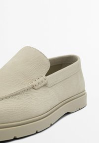Chaussure slip-on texturée beige avec une semelle épaisse et des coutures détaillées le long de la tige, photographiée sur fond blanc.