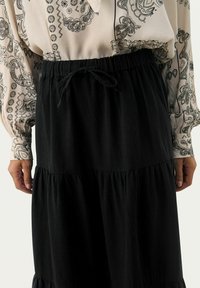 Gonna nera a livelli con una vita elastica e un cordoncino. Abbinata a una blusa color crema con un motivo e dettagli neri.