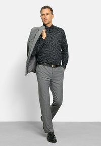 Grauer Blazer über einem schwarz gemusterten Hemd, graue Hose und schwarze Schuhe. Das Outfit zeichnet sich durch eine schmale Passform und ein dezentes Blumenmuster auf dem Hemd aus.