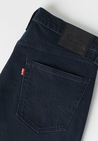 Jean bleu foncé plié pour montrer la poche arrière avec l'étiquette rouge Levi's et l'étiquette en cuir noir sur la ceinture.