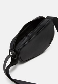 Black synthetic crossbody bag with a rounded rectangular shape, featuring a zipper closure and a detachable woven strap. Smooth texture.