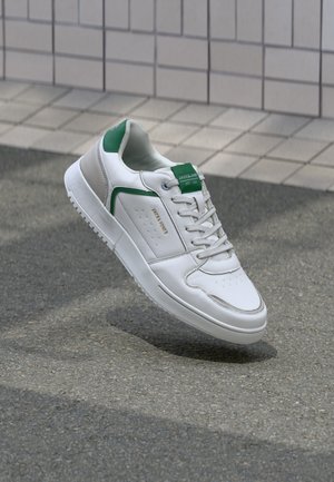 White leather sneaker with green and gray accents, lace-up design, perforated toe, and embossed branding on the tongue. Low-cut silhouette.
