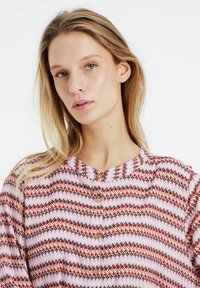 Blusa colorata a motifs con scollo rotondo e chiusura con bottoni. Presenta disegni a zigzag rossi, rosa e neri su uno sfondo chiaro.