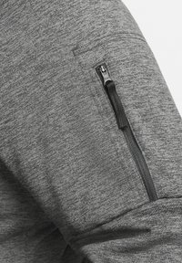 Gros plan d'une manche en tissu gris avec une poche zippée noire présentant une languette en tissu sur la partie supérieure du bras.