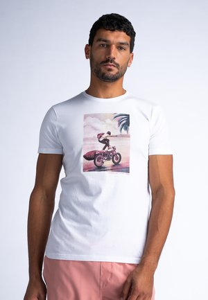 White cotton t-shirt featuring a colorful graphic of a person riding a motorcycle with a surfboard, surrounded by palm trees and clouds.