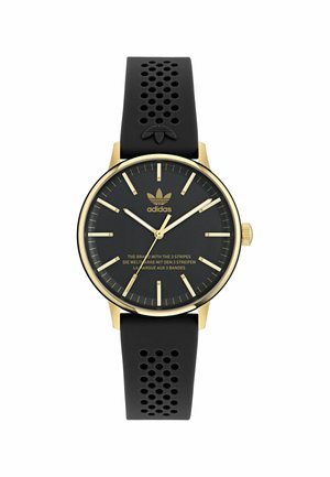 Bracelet en silicone noir avec perforations, boîtier doré, cadran noir, index dorés, et logo de la marque. Présente un design minimaliste.