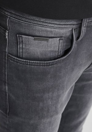 Donkergrijze denim jeans met een achterzak voorzien van een klein zwart label. De stof is zacht met een lichte glans en heeft een minimalistisch ontwerp.