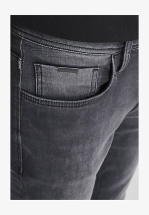 Dunkelgraue Denim-Jeans mit einer Gesäßtasche und einem kleinen schwarzen Etikett. Der Stoff ist weich mit einem leichten Glanz und minimalistischem Design.