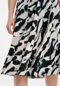Vestido abstracto en negro y verde con tejido fluido, diseño plisado y dobladillo asimétrico, que muestra una textura suave.