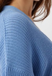 Light blue knit sweater with ribbed texture, featuring a V-neckline and slightly dropped shoulders, showing a close-up view of the shoulder seam.