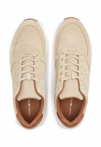 Scarpe da ginnastica beige realizzate in materiali mesh e suede, con punta tonda, lacci piatti e suola bianca con accenti marroni. Logo visibile all'interno.