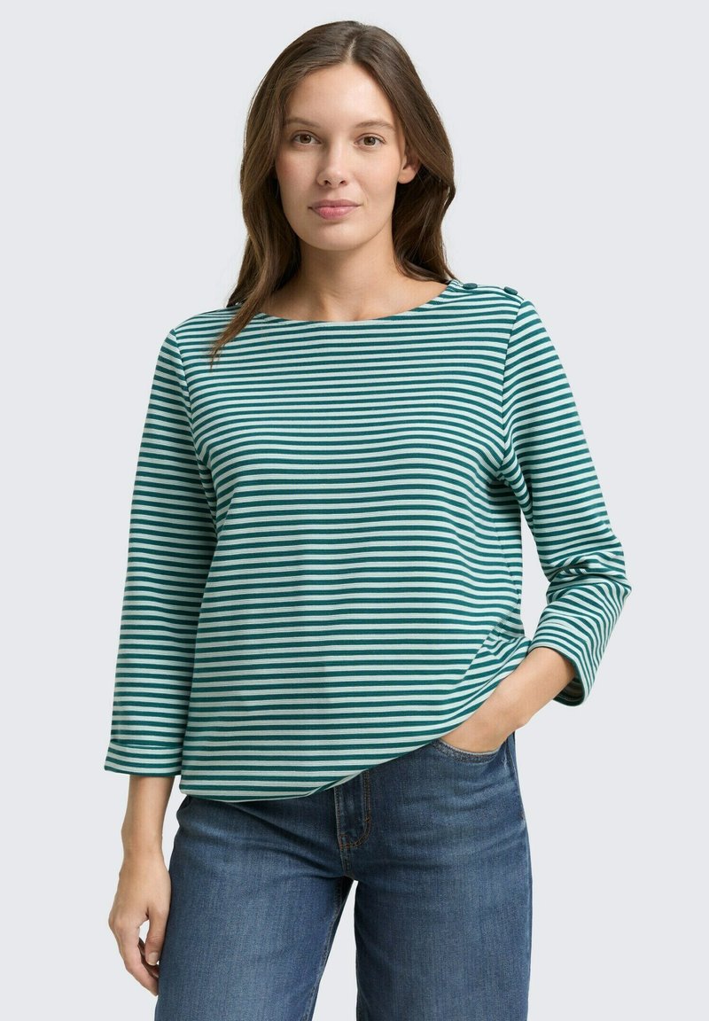 Striped long-sleeve top in teal and white, featuring a round neckline and a slight asymmetrical hem, worn with blue jeans.