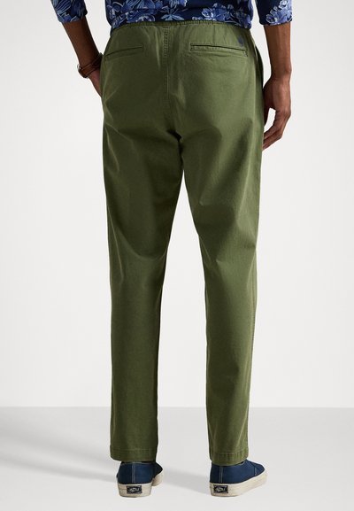 Πράσινα βαμβακερά παντελόνια με χαλαρή εφαρμογή, που διαθέτουν δύο πίσω τσέπες και λεία, ματ υφή, συνδυασμένα με ναυτικές κα casual παπούτσια.