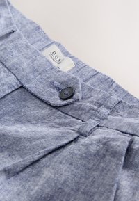 Sinised tekstuurse kangaga lühikesed püksid vöökohaga, millel on üks must nööp ja sees kinnitatud silt tekstiga "next".