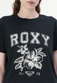 Black cotton t-shirt featuring "ROXY" in distressed white letters, with a floral graphic and "Est. 90" in white below a heart logo.