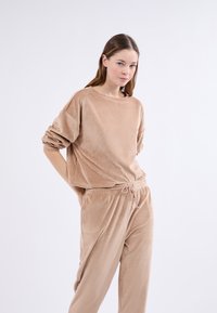 Beżowy zestaw odzieży dresowej z korduroju, składający się z luźnej bluzki z długim rękawem i opuszczonymi ramionami oraz spodni z elastycznym pasem i sznurkiem do regulacji.