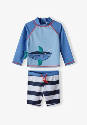 Modrý plavkový set s topom s dlhým rukávom, ktorý má dizajn žraloka a červené akcenty. Zodpovedajúce šortky s námorníckymi a bielymi horizontálnymi pruhmi.
