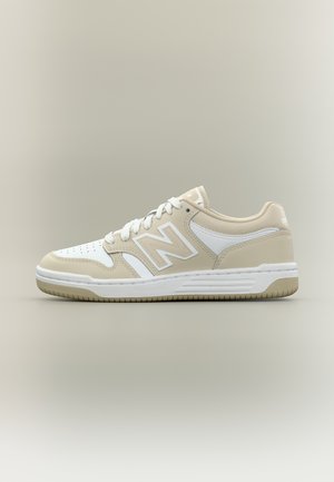 Pantof sport bej și alb, de tip low-top, cu vârf perforat, logo "N" pe lateral, șireturi albe și talpă texturată pe fundal neutru.