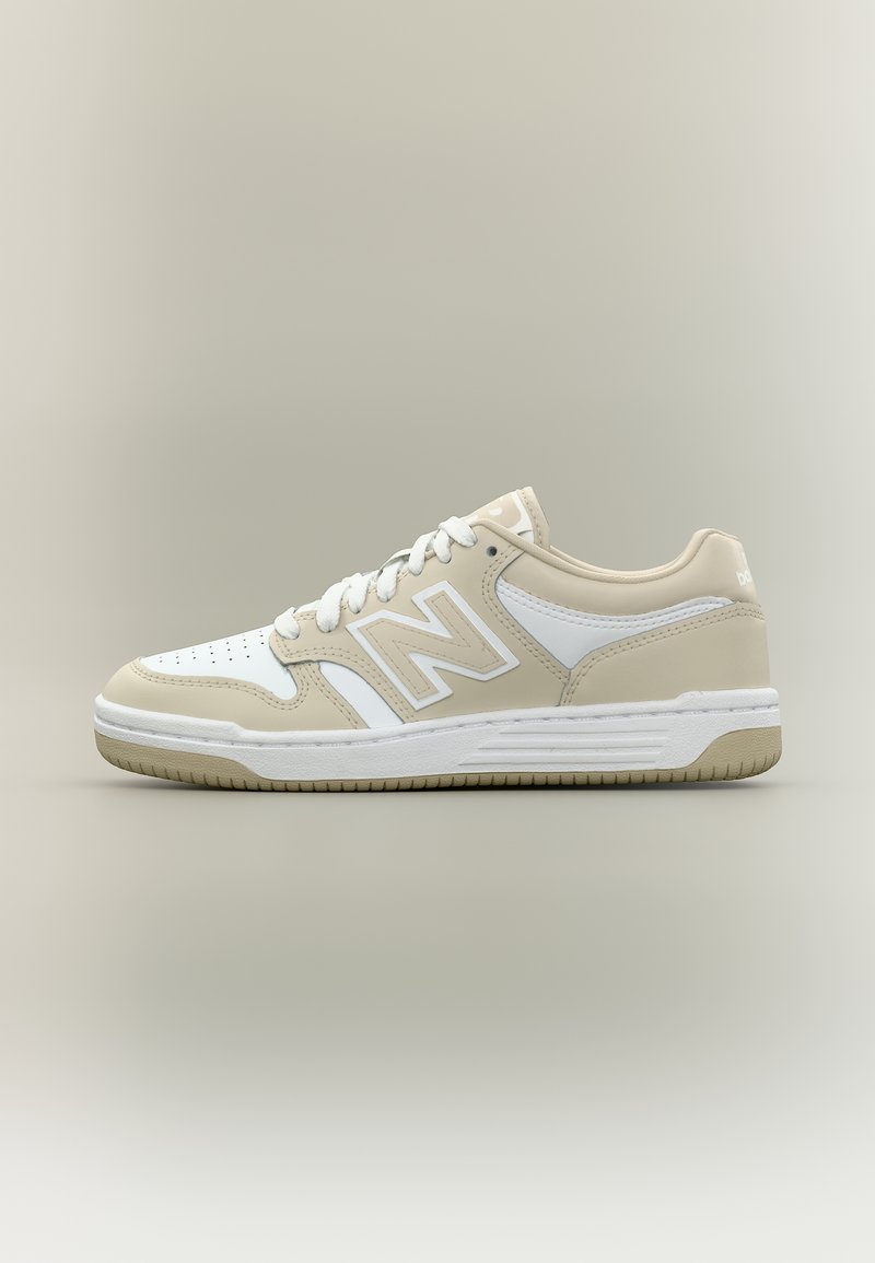 Béžová a bílá nízká teniska s perforovanou špičkou, logem "N" na boku, bílými tkaničkami a strukturovanou podrážkou na neutrálním pozadí.